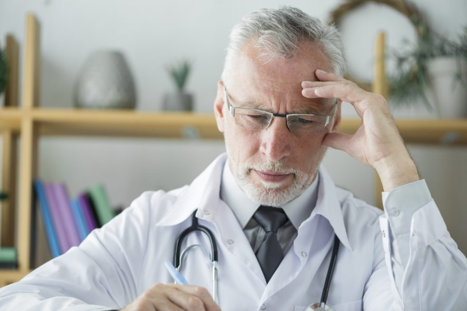 senior-doctor-thinking-writing-office