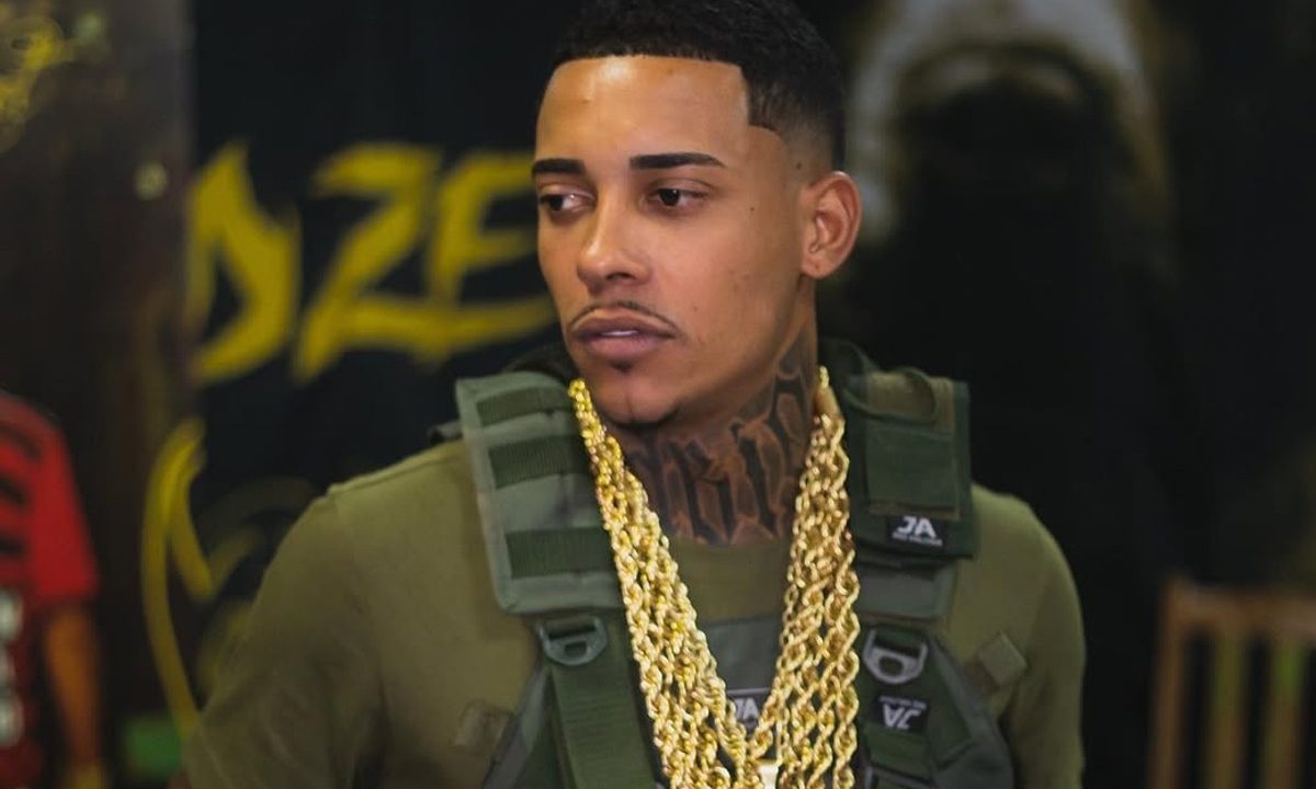 Foto do cantor MC Poze olhando para o lado; artista está com colete e cordões de ouro