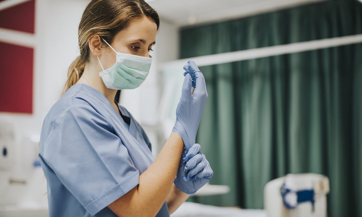Female nurse with a mask putting on gloves