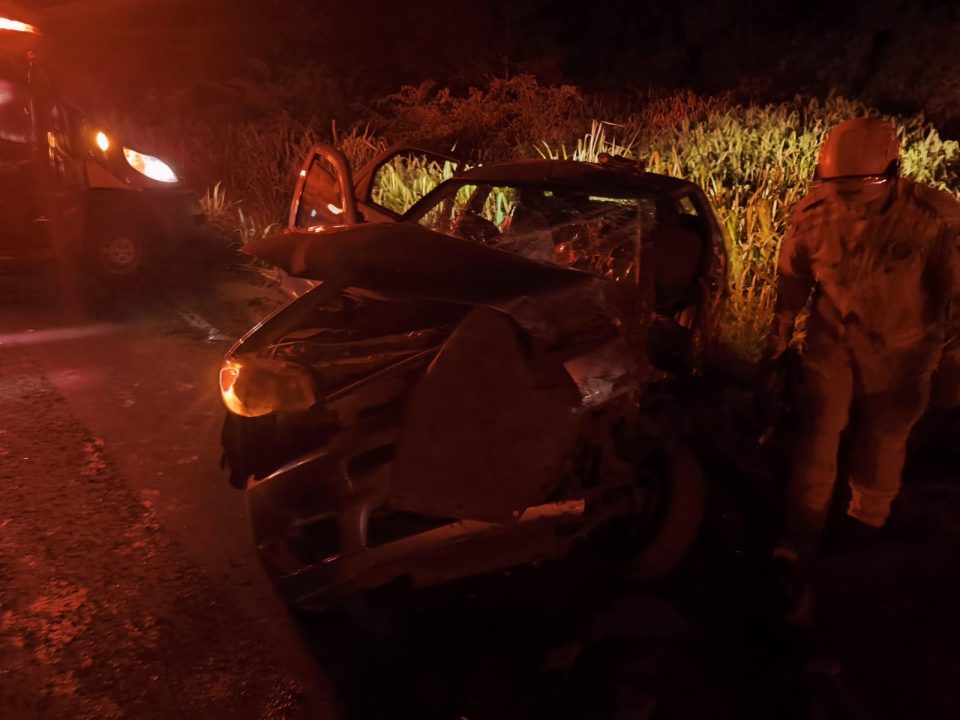 Foto mostra carro destruído após colisão contra caminhão-tanque. O veículo Siena tem cor cinza e a foto foi tirada à noite