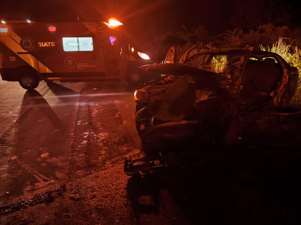 Foto mostra carro destruído após colisão contra caminhão-tanque. O veículo Siena tem cor cinza e a foto foi tirada à noite