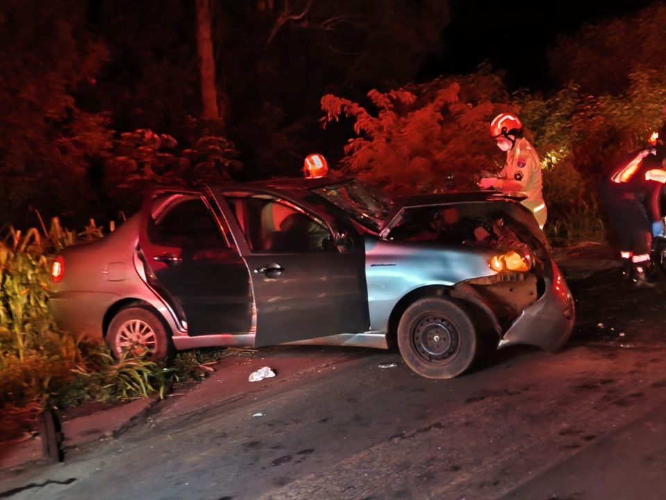 Foto mostra carro destruído após colisão contra caminhão-tanque. O veículo Siena tem cor cinza e a foto foi tirada à noite