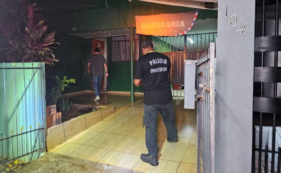 Foto mostra dois policiais entrando na casa da vítima morta após o crime. A casa é verde
