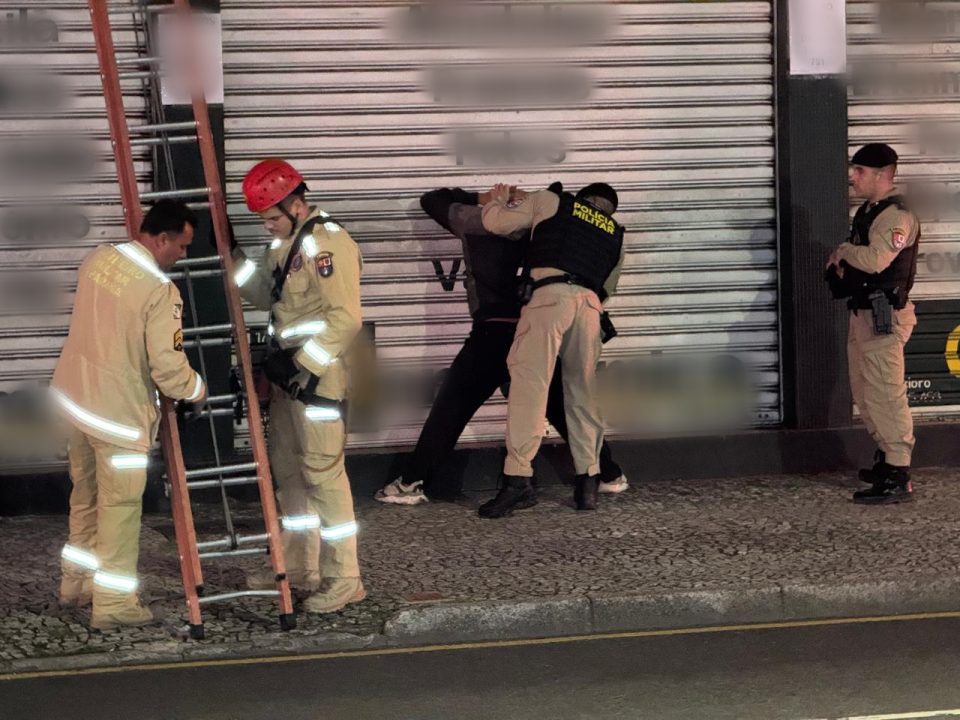 Foto mostra policiais militares revistando suspeito preso ao lado de bombeiros