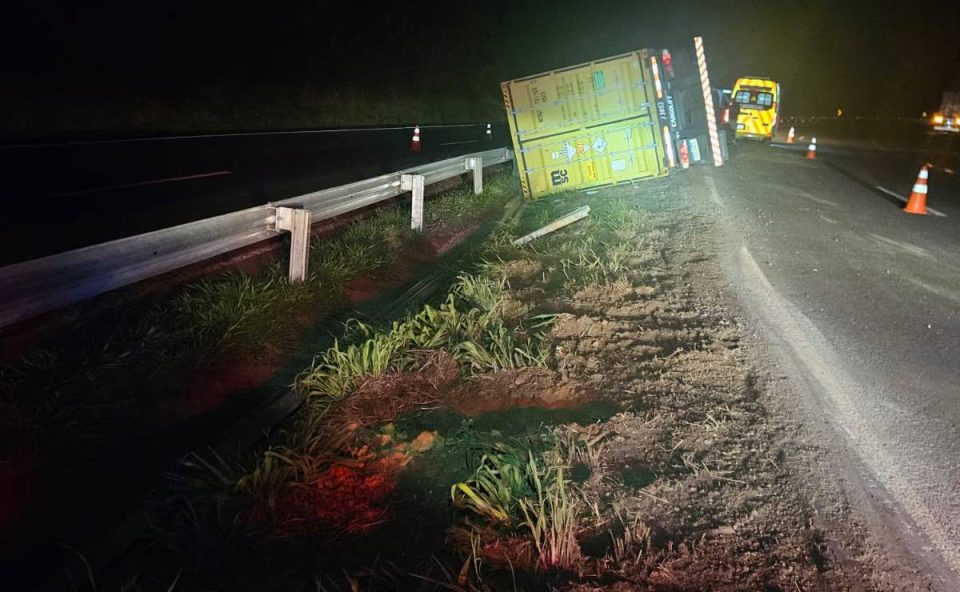Foto mostra caminhão tombado sobre canteiro na pista na BR-376