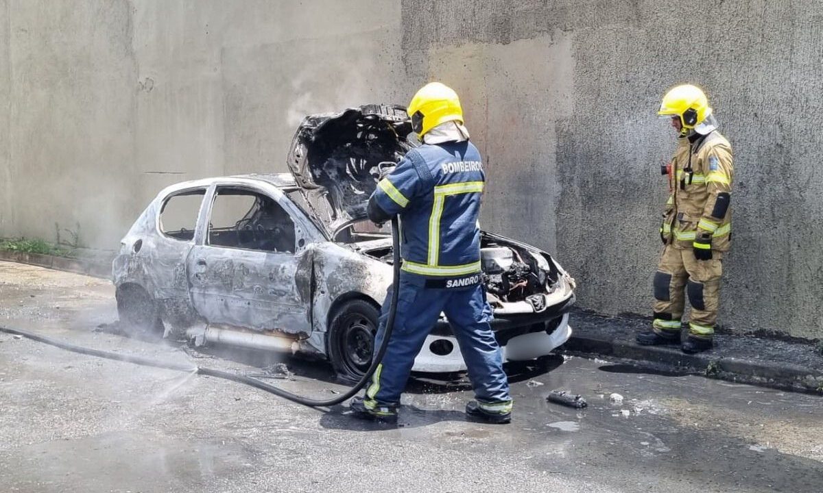 Carro destruído após pegar fogo e bombeiros controlando incêndio