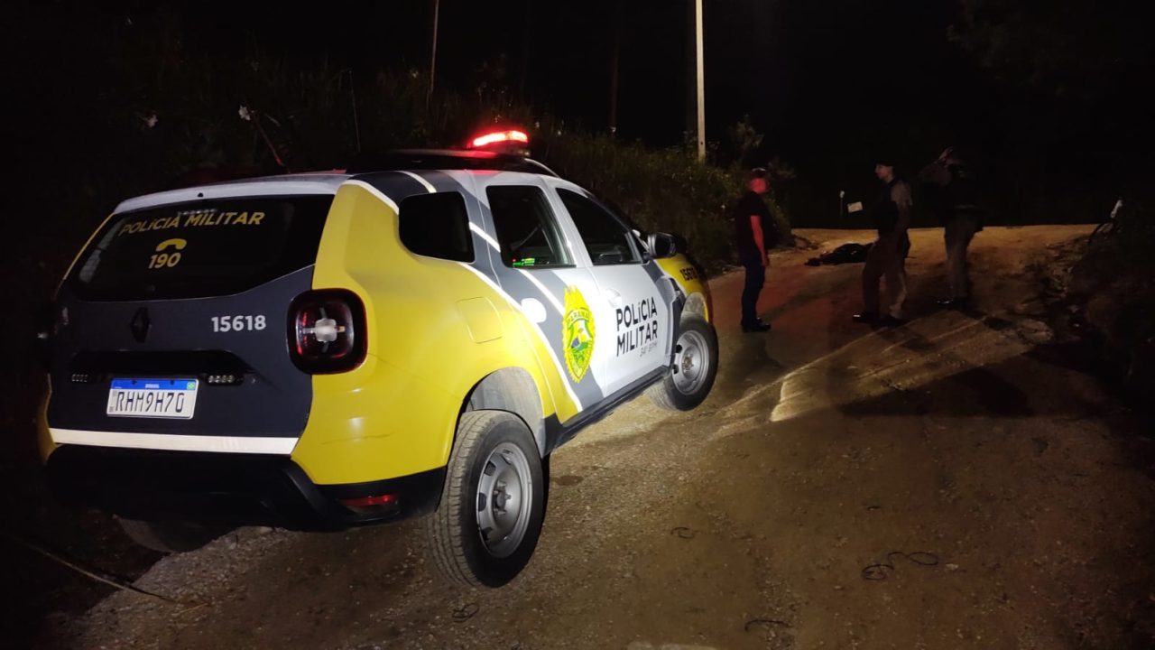 Viatura da Polícia Militar na rua escura em Almirante Tamandaré, após ataque a tiros que deixou um homem morto e uma mulher ferida.