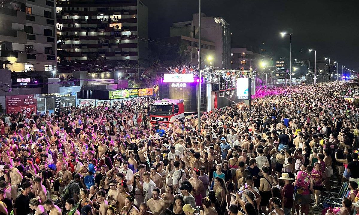 Foto mostra milhares de pessoas aproveitando o Carnaval na praia com um trio elétrico
