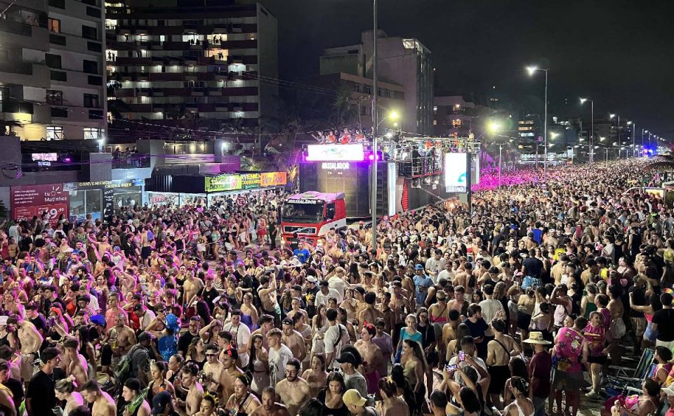 Foto mostra milhares de pessoas aproveitando o Carnaval na praia com um trio elétrico