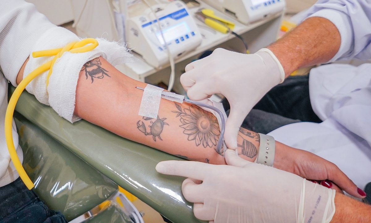 Profissional de saúde realiza coleta de sangue em braço de doador durante procedimento em hemocentro.