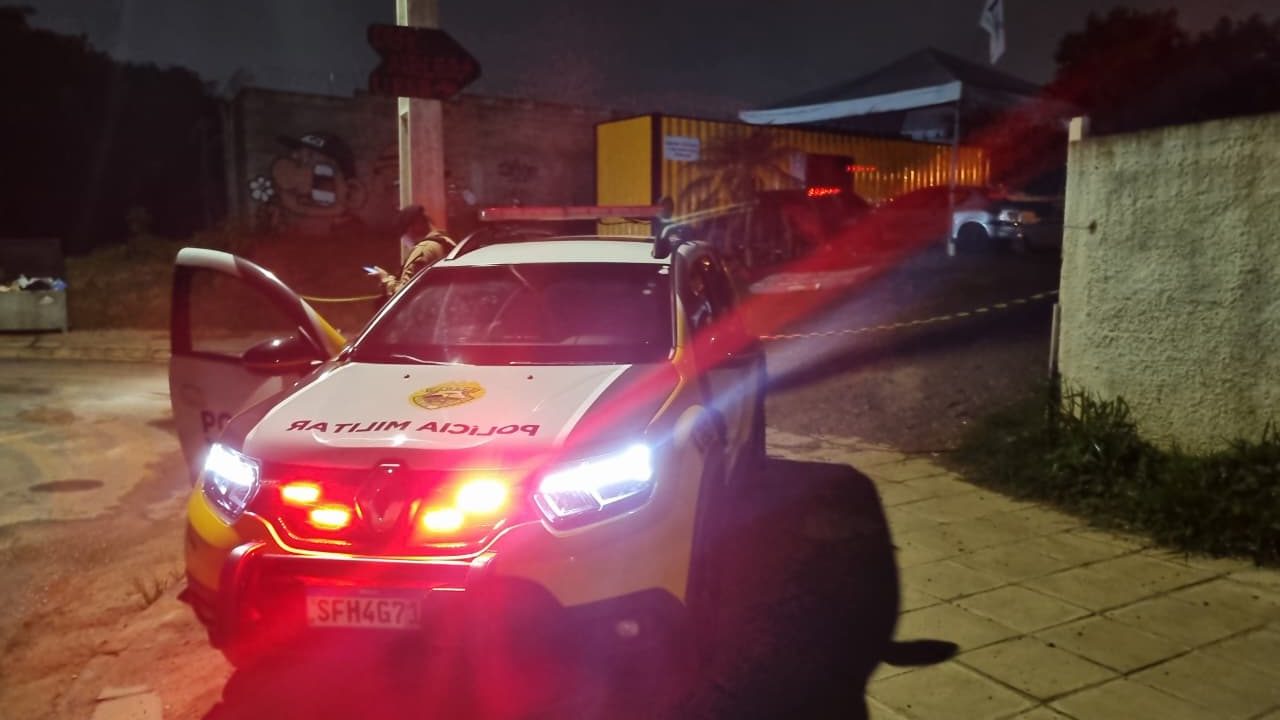 Foto tirada à noite mostra viatura da Polícia Militar, com sinais luminosos, parada em frente ao local onde homem foi executado com tiro na cabeça