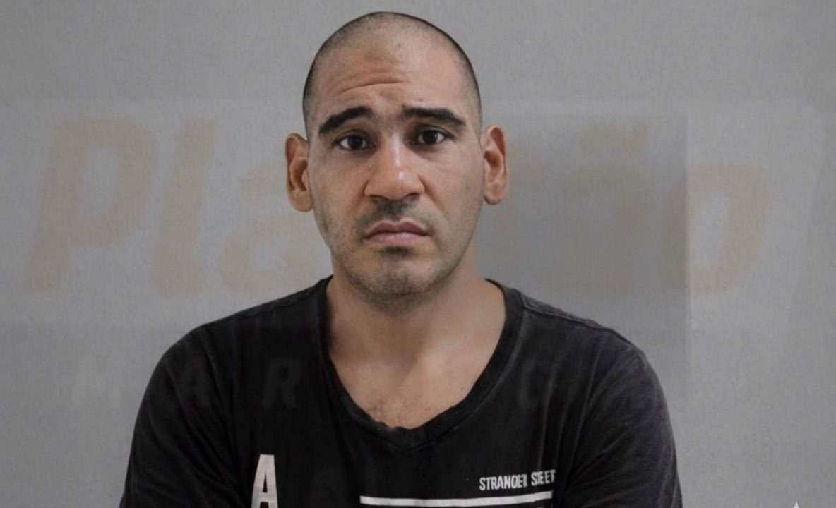 Foto mostra César Rodrigues dos Santos um homem careca e barba feita, posando para foto sem sorrir. Atrás dele há uma parede cinza. Ele usa uma camiseta preta com estampa.