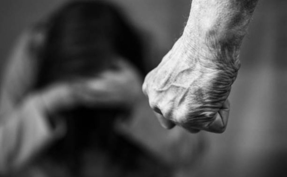 Homem com a mão em formato de soco enquanto mulher se esconde ao fundo