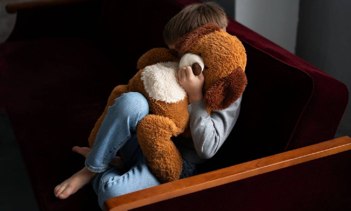 Foto mostra criança com medo segurando urso de pelúcia
