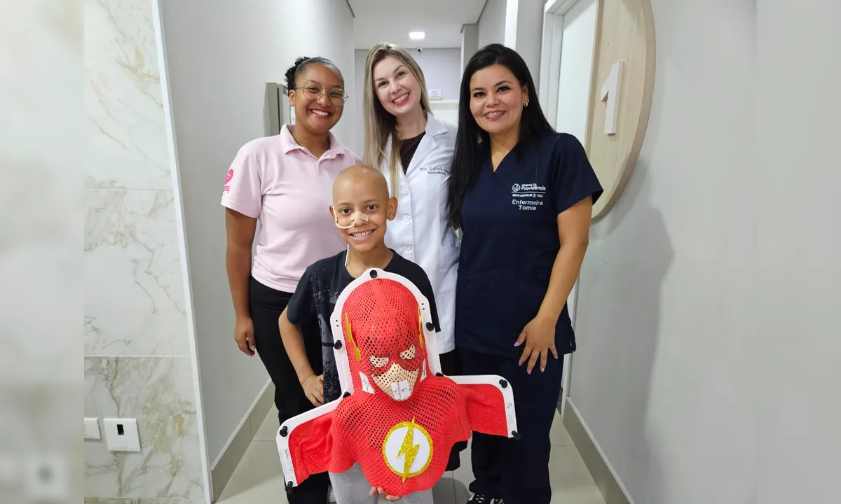 Vitor Gabriel de Souza, de 10 anos faz tratamento de radioterapia e ganhou uma máscara personalizada. A criança está no hospital acompanhado de um responsável e da equipe de saúde.
