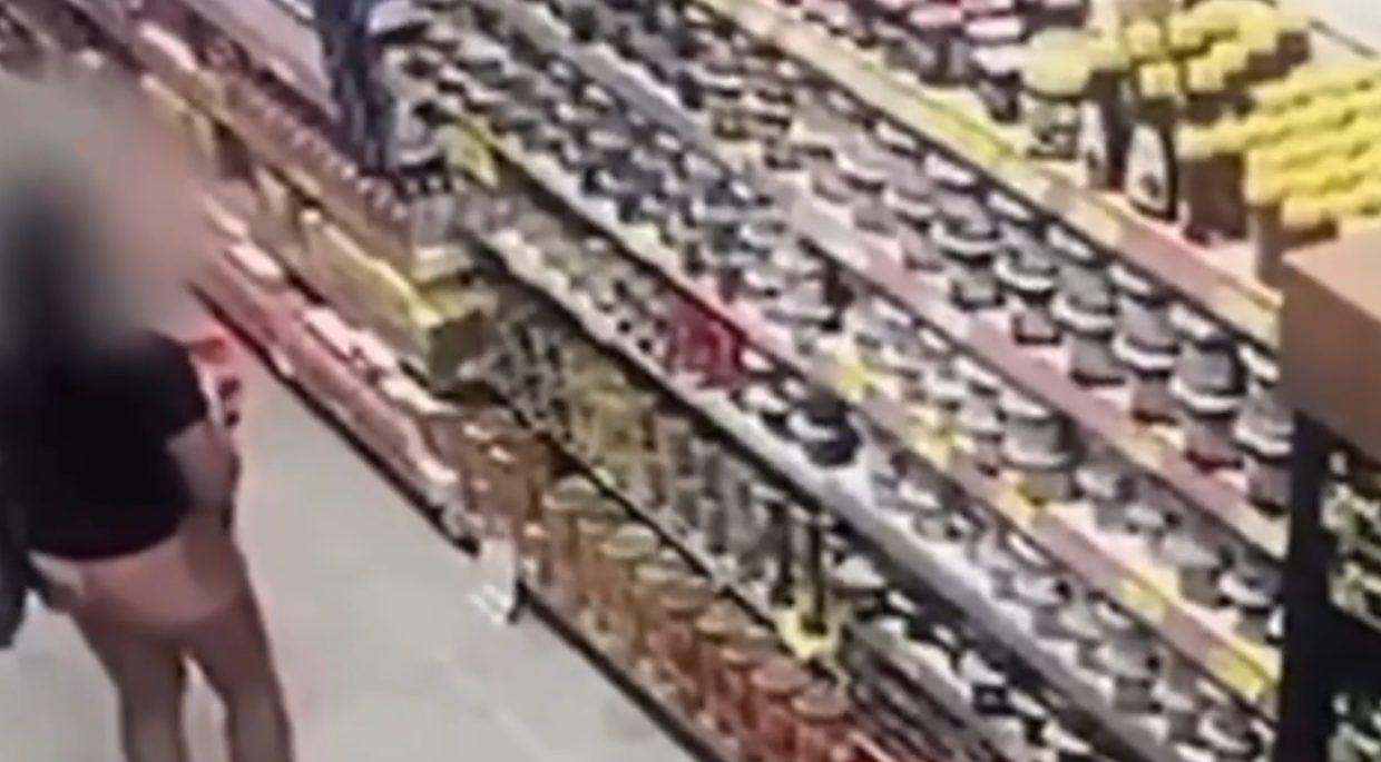 Frame de vídeo mostra mulher parada diante de produtos posicionados em uma prateleira de supermercado. O rosto dela foi borrado por meio de edição. Ela foi presa sob a suspeita de furtar potes de avelã.