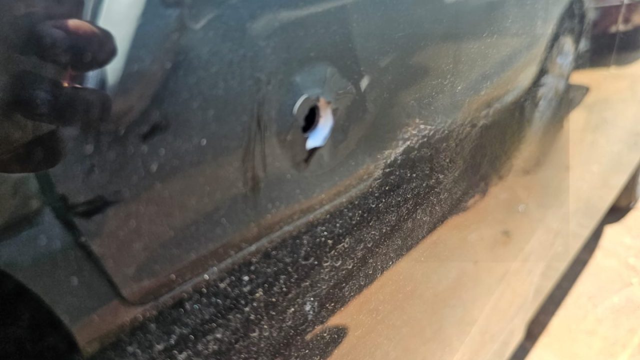 Foto tirada durante o dia mostra marca de tiro em lataria de carro preto