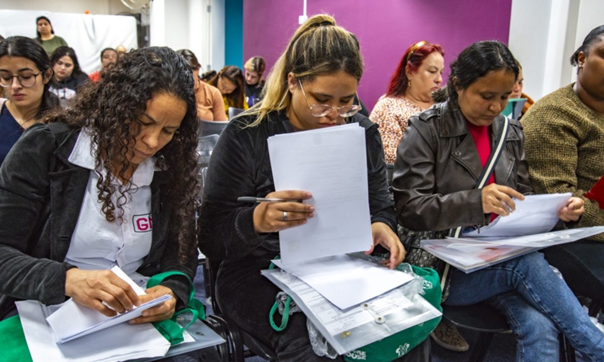 Candidatos analisando documentos e computador para inscrição em processo seletivo.
