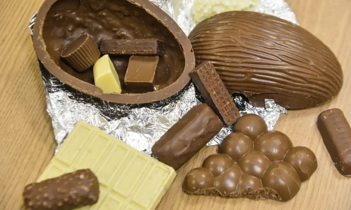 Chocolates em cima da mesa. Dois em formato de ovo de páscoa, alguns pedacos de chocolate preto e um tablete branco
