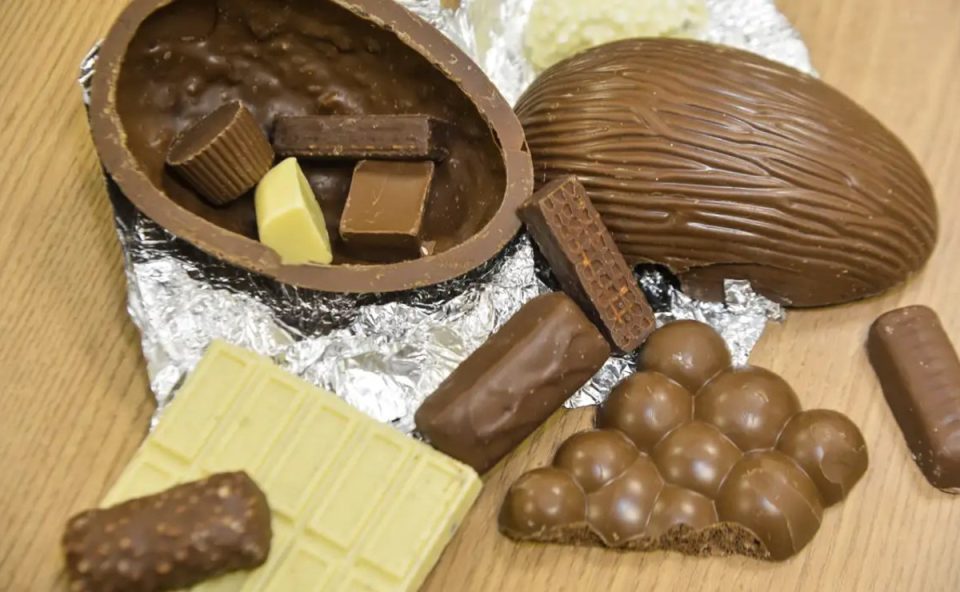 Chocolates em cima da mesa. Dois em formato de ovo de páscoa, alguns pedacos de chocolate preto e um tablete branco