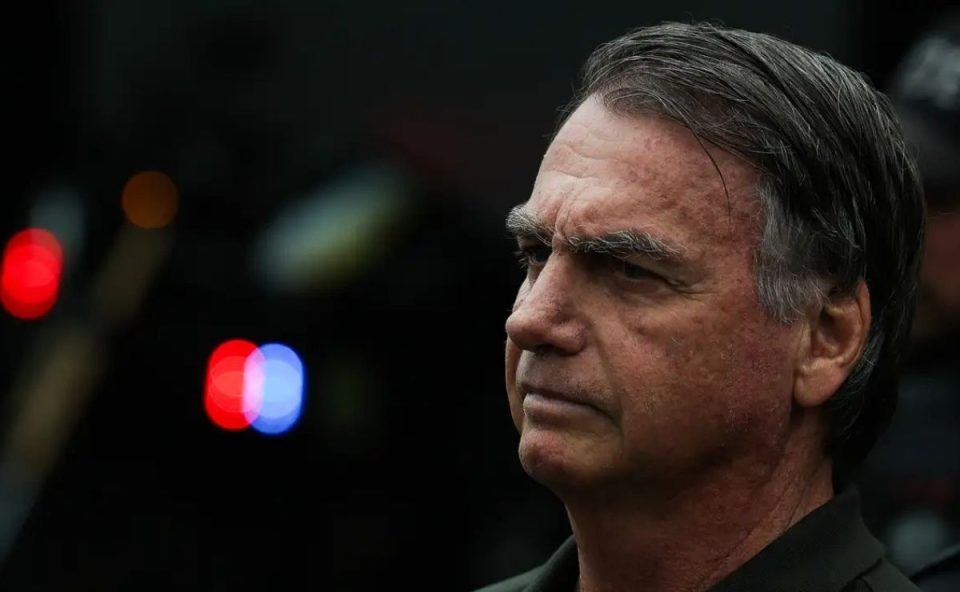 Foto de perfil do ex-presidente Jair Bolsonaro olhando para o horizonte, com luzes desfocadas ao fundo. Imagem relativa à notícia de alta hospitalar de Bolsonaro