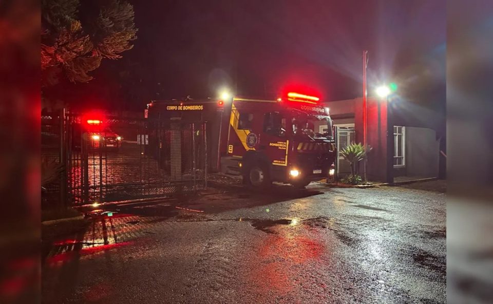 cAMINHÃO DE BOMBEIROS COM LUZES ACESAS PASSANDO POR UM PORTÃO