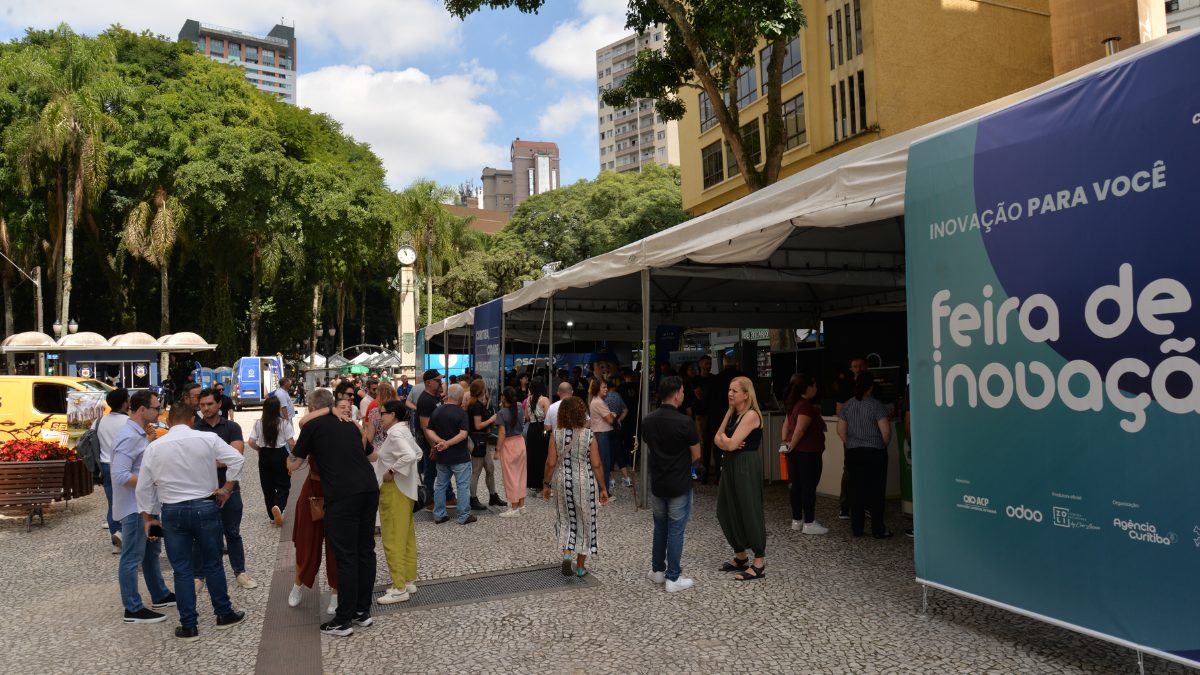 Feira de Inovação no centro de Curitiba durante a celebração de Curitiba 333 anos, com banner informativo e pessoas circulando entre tendas.
