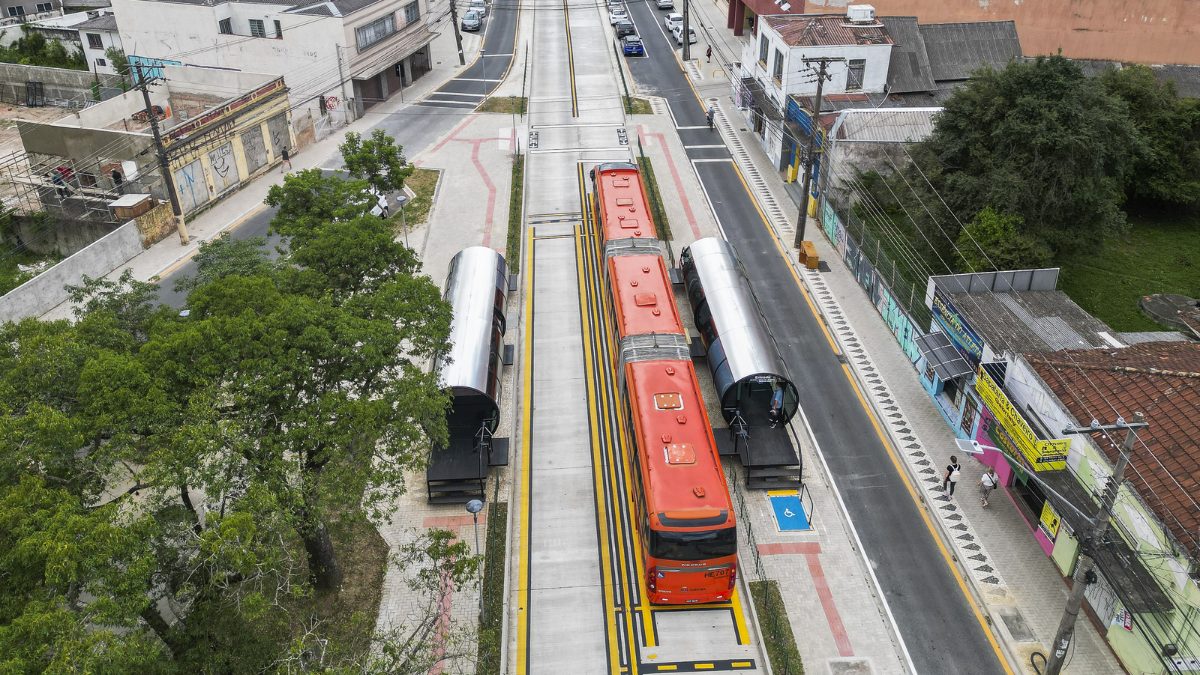 Vista aérea de um terminal de ônibus circular com tubos prateados no centro de Curitiba, com um ônibus articulado laranja, ilustrando a infraestrutura urbana moderna nos Curitiba faz 333 anos.