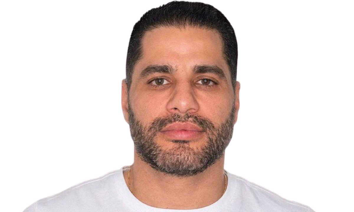 homem branco de cabelo castanho e barba aparada vestindo camiseta branca sobre fundo branco