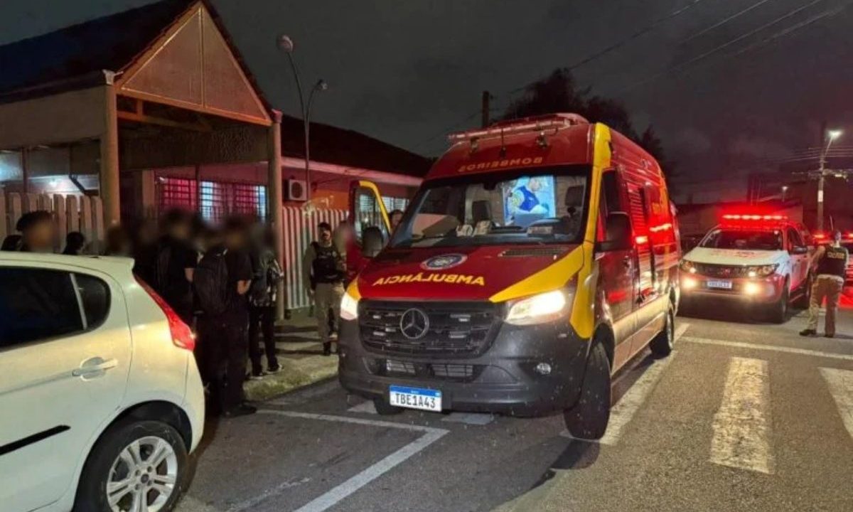 Imagem mostra uma ambulância do Site e outra do Samu em frente ao colégioem Pinhais onde aluno realizou importunação sexual contra uma menina. Ambulância é vermelha e a outra branca e vermelha. Há diversos policiais em frente à instituição.