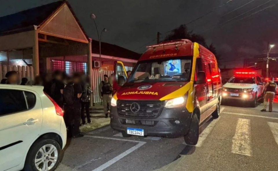 Imagem mostra uma ambulância do Site e outra do Samu em frente ao colégioem Pinhais  onde aluno realizou importunação sexual contra uma menina. Ambulância é vermelha e a outra branca e vermelha. Há diversos policiais em frente à instituição.