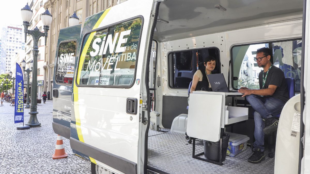 Unidade móvel do SINE Curitiba estacionada no Calçadão da Rua XV de Novembro, com dois atendentes trabalhando em notebooks dentro de uma van branca personalizada