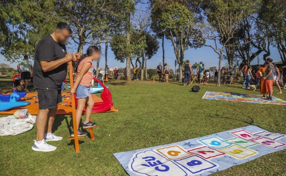 Criança e adultos em um parque de Curitiba brincando em atividades gratuitas disponibilizadas pela Prefeitura.