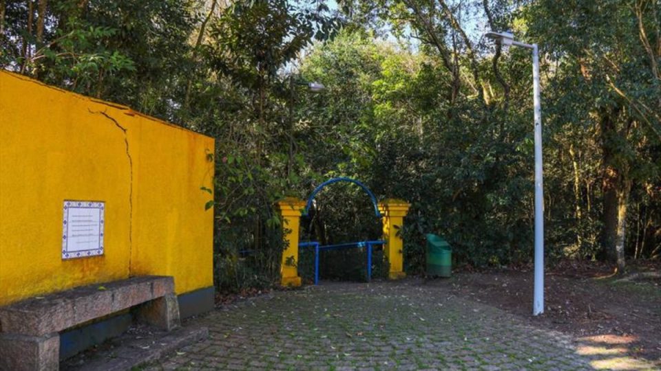 Entrada do Bosque de Portugal com portal amarelo e azul cercado por vegetação densa e caminho de pedras.