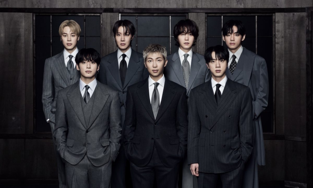 Foto de grupo do BTS (RM, Jin, Suga, J-Hope, Jimin, V, Jungkook) posando juntos em um cenário industrial, vestindo ternos e gravatas para o lançamento do álbum Arirang.