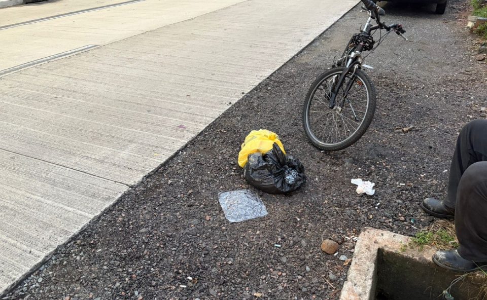 Foto mostra bicicleta parada no asfalto, com sacolas no chão, após ciclista ser atingido por van em avenida de Curitiba