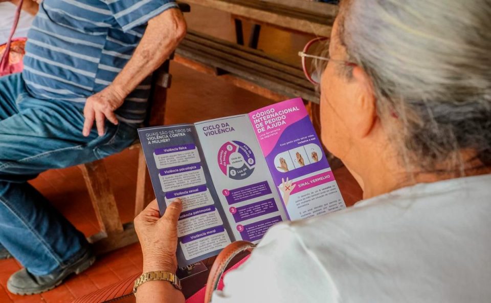 Idosa observa cartilha sobre violência contra a mulher e código internacional de pedido de ajuda