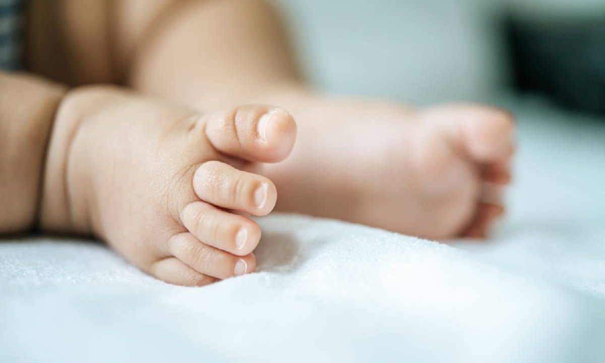 Foto mostra pé de bebê deitado na cama