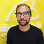 Erick Mota em frente ao fundo com o logo do portal Banda B e parede amarela