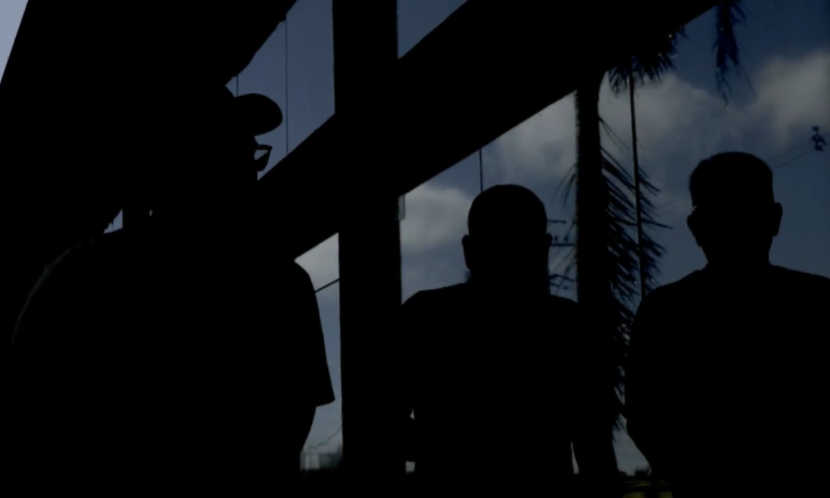 Silhuetas de três homens em ambiente interno, contra a luz, sem identificação, usadas para ilustrar denúncia de golpe.