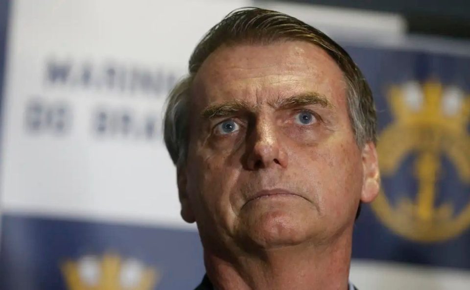 A imagem mostra o rostode Bolsonaro e, ao fundo, a logo da Marinha do Brasil desfocada.