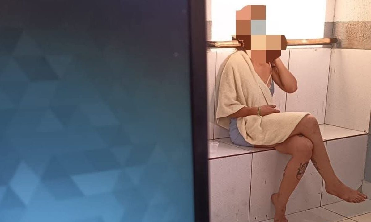 Mulher que tirou a roupa diante de guardas é vista sentada em um banco dentro da delegacia, envolta em um roupão, após ser detida pela Guarda Civil Municipal.