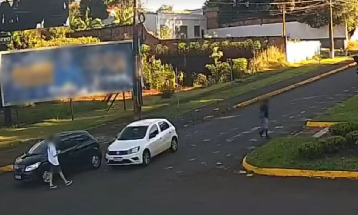 Dois carros, um branco e um preto, aparecem parados em uma rua de Marechal Cândido Rondon enquanto homens observam o local onde homem morre em confronto com a PM após roubo de carro.