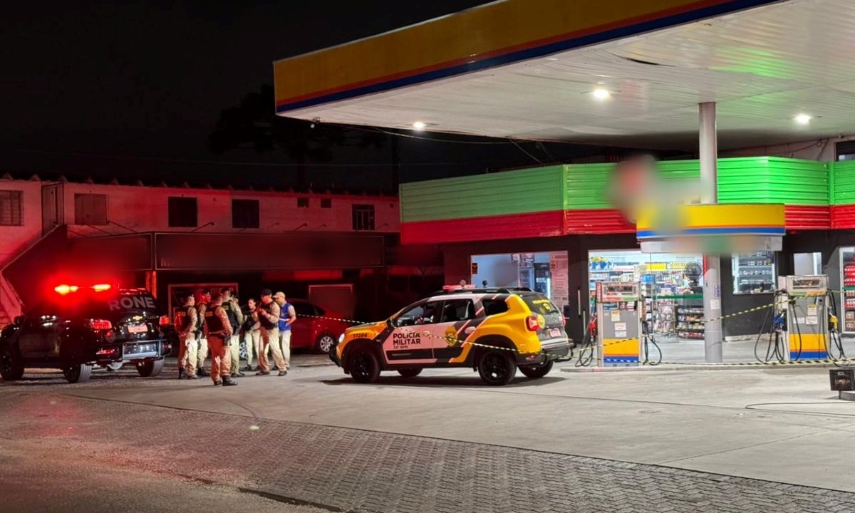 Foto mostra uma viatura da Polícia Militar parada dentro do posto de combustível e policiais conversando, onde homem foi morto a tiros enquanto esperava a esposa, em Colombo