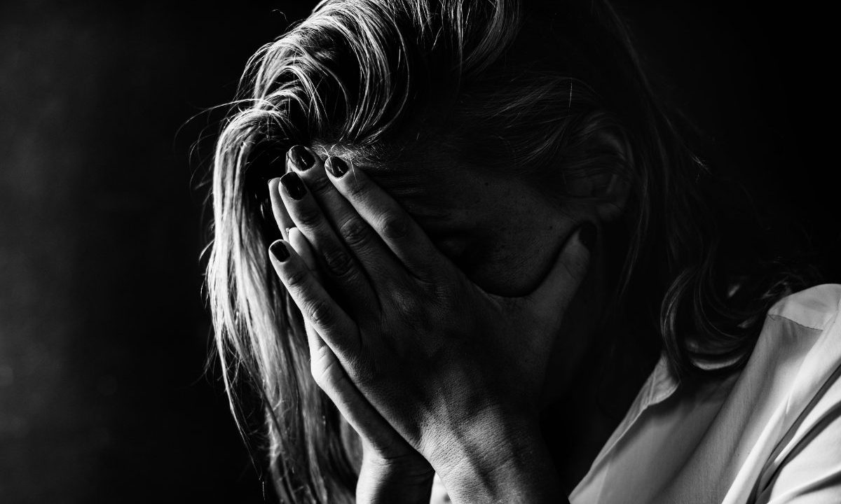 Homem é preso por manter esposa em cárcere privado. Imagem mostra uma mulher com as mãos no rosto.