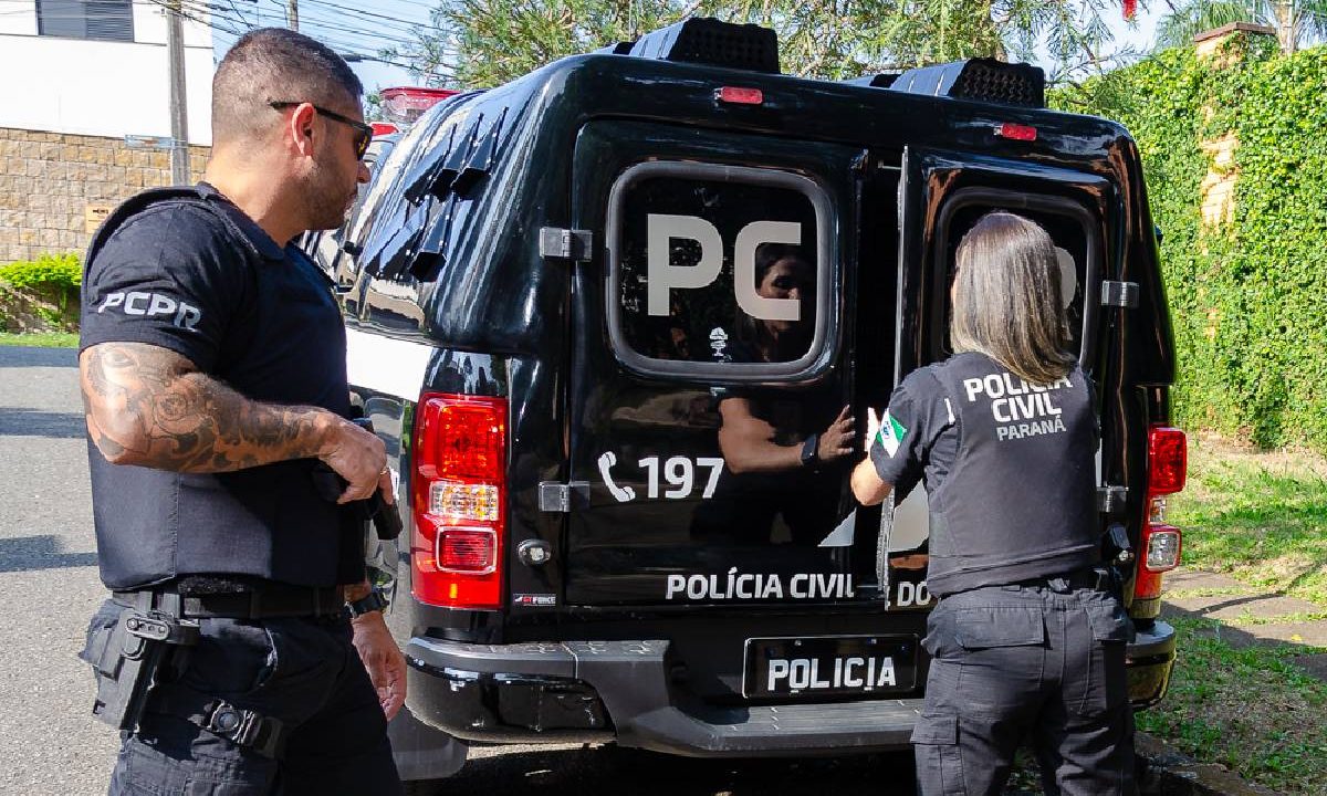 Foto mostra policiais fechando viatura