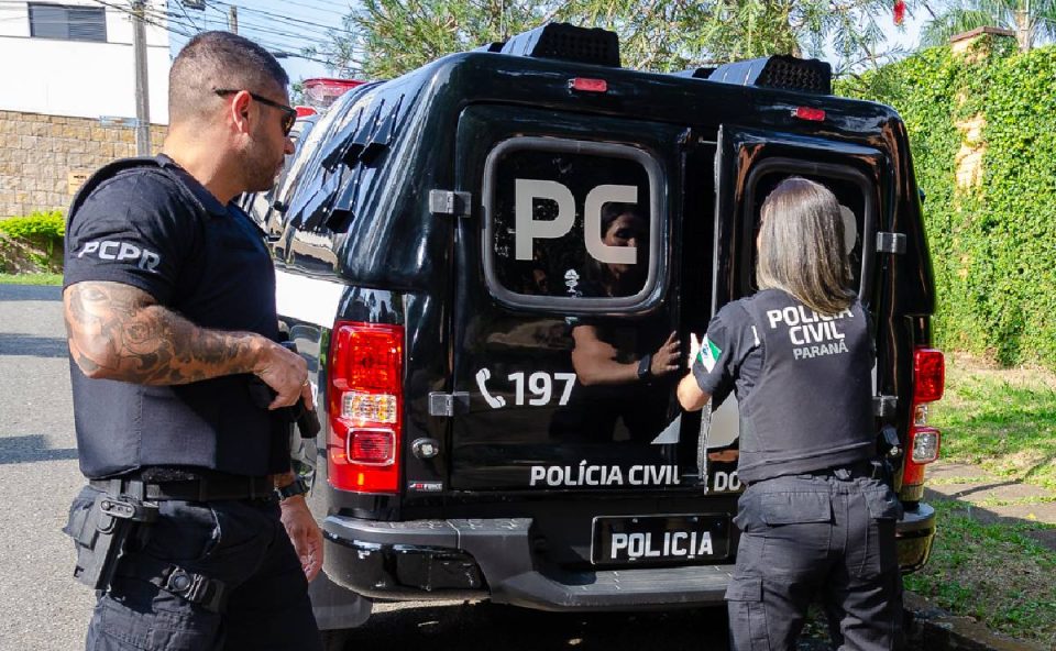 Foto mostra policiais fechando viatura