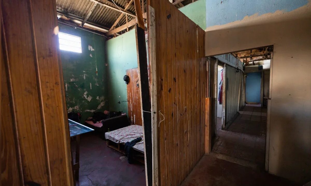 Quarto de madeira em pensionato onde jovem com tornozeleira eletrônica foi encontrado morto, com estrutura simples e aspecto precário no interior do imóvel.