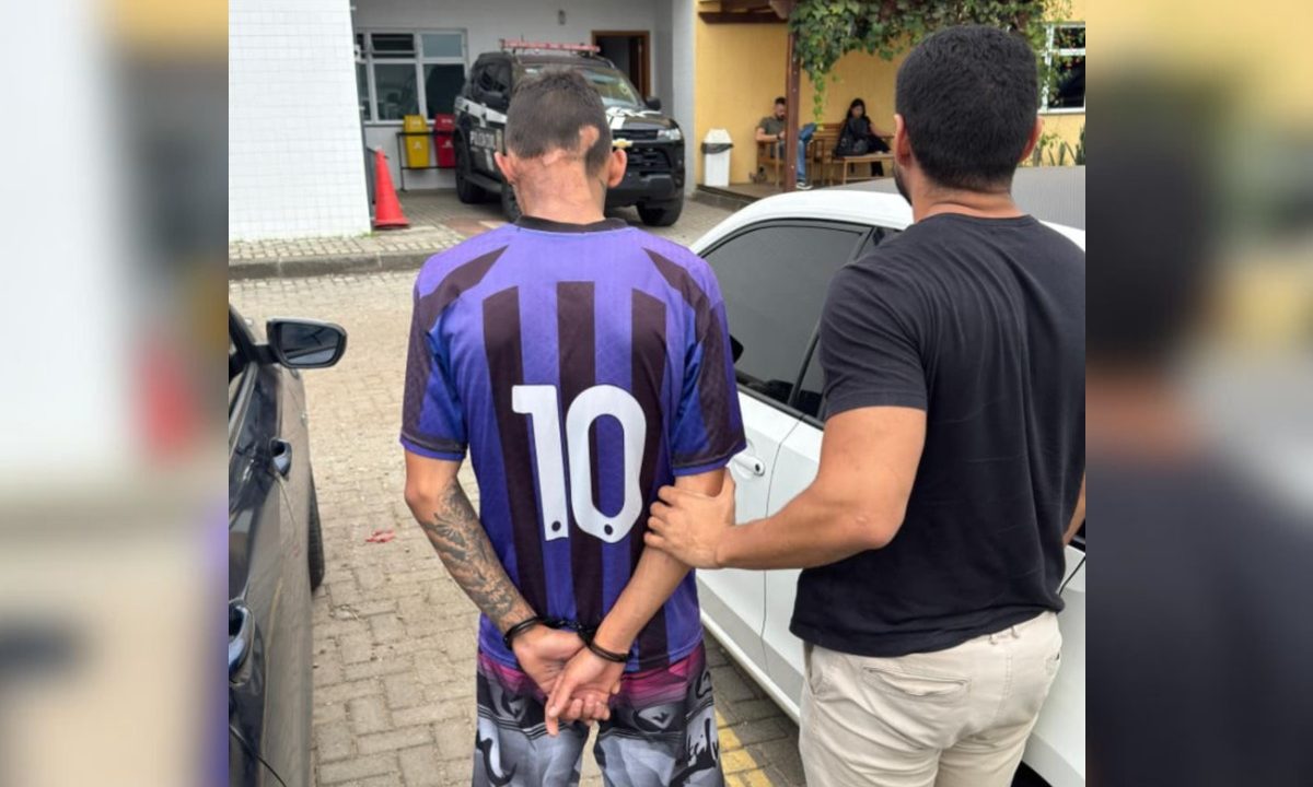 Jovem sendo levado por policial até a delegacia após ser preso por tentar matar dois homens a tiros por causa de uma vassoura em Curitiba.