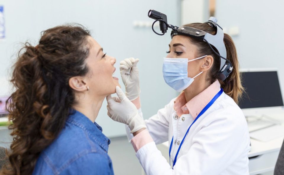 Médica otorrinolaringologista examina a garganta de paciente durante consulta examinando possíveis causas do mau hálito